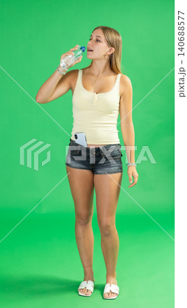 Teenage girl drinking water in front of green screen Teenage girl drinking water in front of green screen 140688577