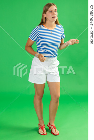 Girl in white shorts looks around, searching for something on green background. Girl in white shorts looks around, searching for something on green background. 140688625