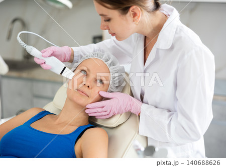 Young female cosmetologist doing exfoliating procedure to adult woman Young female cosmetologist doing exfoliating procedure to adult woman 140688626