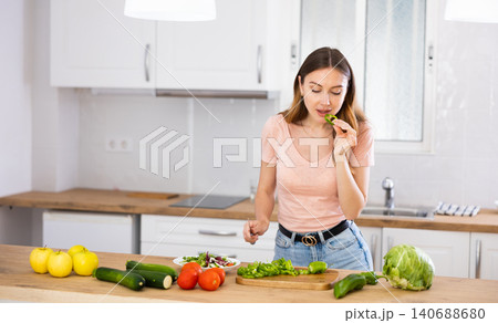 Woman tasting vegetable while cooking salad at home 140688680