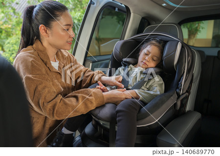 mother is fastening safety belt to preschool child girl while sleeping in car seat, safety baby chair travelling mother is fastening safety belt to preschool child girl while sleeping in car seat, safety baby chair travelling 140689770