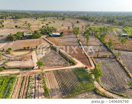 Aerial view of cultivated farmland with crop rows, rural roads, ponds, and scattered farmhouses. Agricultural production and sustainable land management. Sustainable agriculture and rural development. 140689798
