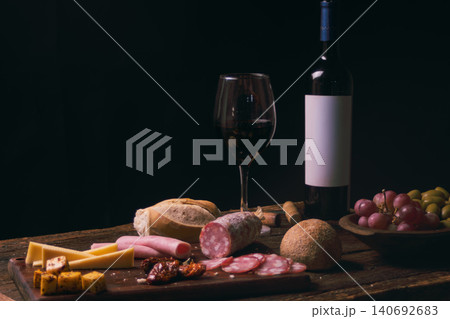 Red wine and assorted gourmet charcuterie board with sliced cheeses, salami, ham, bread, olives, and grapes, creating a luxurious still life tasting experience 140692683