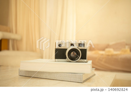 A vintage camera rests on stacked books in a warm space A vintage camera rests on stacked books in a warm space 140692824