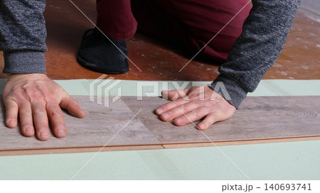 The process of installing flooring in a room yourself. The technician lays laminate or quartz vinyl panels in a gray-brown color with a distinct natural wood texture The process of installing flooring in a room yourself. The technician lays laminate or quartz vinyl panels in a gray-brown color with a distinct natural wood texture 140693741