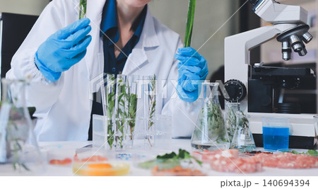 Scientists in lab coats work with plants in a modern lab, focusing on research and experimentation under bright, sterile conditions. Scientists in lab coats work with plants in a modern lab, focusing on research and experimentation under bright, sterile conditions. 140694394