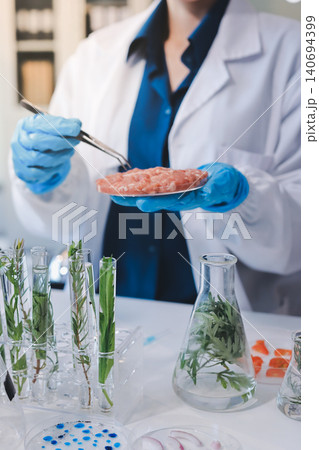 Scientists in lab coats work with plants in a modern lab, focusing on research and experimentation under bright, sterile conditions. Scientists in lab coats work with plants in a modern lab, focusing on research and experimentation under bright, sterile conditions. 140694399