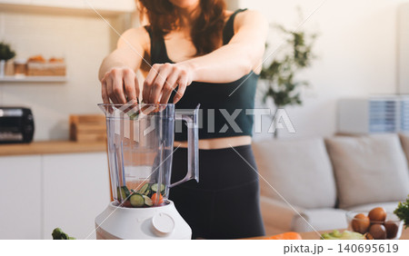 Woman preparing green smoothie in bright kitchen with fresh fruits and vegetables, healthy eating lifestyle moment in natural daylight Woman preparing green smoothie in bright kitchen with fresh fruits and vegetables, healthy eating lifestyle moment in natural daylight 140695619