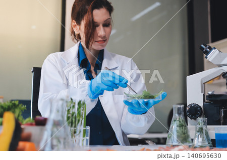 Scientists in lab coats work with plants in a modern lab, focusing on research and experimentation under bright, sterile conditions. Scientists in lab coats work with plants in a modern lab, focusing on research and experimentation under bright, sterile conditions. 140695630