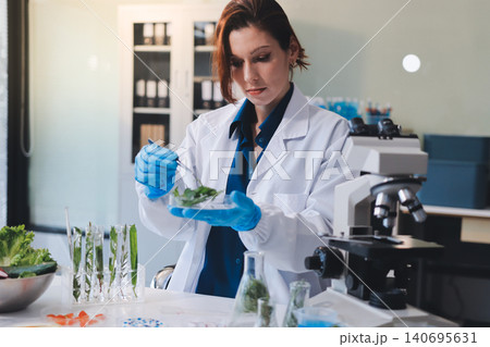 Scientists in lab coats work with plants in a modern lab, focusing on research and experimentation under bright, sterile conditions. Scientists in lab coats work with plants in a modern lab, focusing on research and experimentation under bright, sterile conditions. 140695631