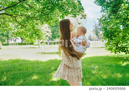 Mother plays with baby in park on sunny day near trees and grass Mother plays with baby in park on sunny day near trees and grass 140695666