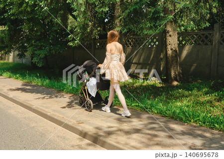 Unrecognizable woman walks with stroller along sidewalk in sunny day near trees Unrecognizable woman walks with stroller along sidewalk in sunny day near trees 140695678