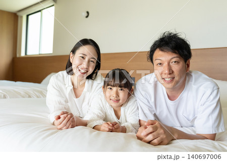 明るい寝室のベッドでくつろぐ笑顔の3人家族 明るい寝室のベッドでくつろぐ笑顔の3人家族 140697006