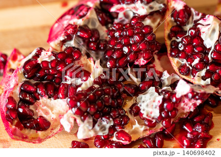 Close up of pieces of cutted fresh pomegranate on a wooden table. Bright red seeds of pomegranate, juicy tasty fruit, full of vitamins Close up of pieces of cutted fresh pomegranate on a wooden table. Bright red seeds of pomegranate, juicy tasty fruit, full of vitamins 140698402