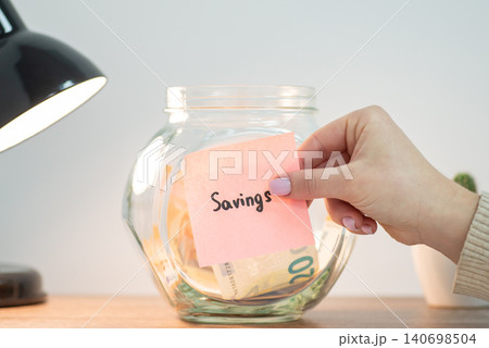 Female putting paper with inscription Savings on jar with euro money. Saving money, savings for education, purchase of house or car Female putting paper with inscription Savings on jar with euro money. Saving money, savings for education, purchase of house or car 140698504