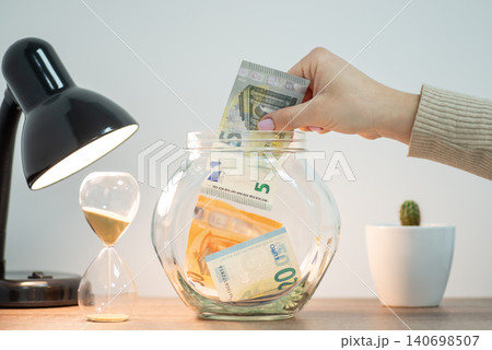 Saving money in Europe concept. Woman putting 5 euro banknote to jar Saving money in Europe concept. Woman putting 5 euro banknote to jar 140698507