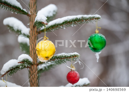 Top of the small fir tree covered with snow and having Christmas toys on its branches, outdoors. Colorful decoration, bright balls in ice, time of winter holidays Top of the small fir tree covered with snow and having Christmas toys on its branches, outdoors. Colorful decoration, bright balls in ice, time of winter holidays 140698569
