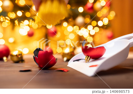 Red christmas ball is broken, laying on white scoop, close up. Cleaning from the floor sharp pieces of a broken glass christmas tree decoration 140698573