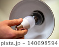 White LED light bulb in male`s hand, holding it near the the lamp with incandescent bulb. Changing the house lightning, concept of energy-efficiency 140698594
