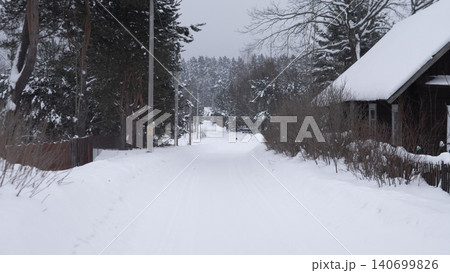 Empty snow covered lane leading through small village with wooden houses and timber fences on both sides, tall conifer and birch trees dusted with snow, dense Empty snow covered lane leading through small village with wooden houses and timber fences on both sides, tall conifer and birch trees dusted with snow, dense 140699826