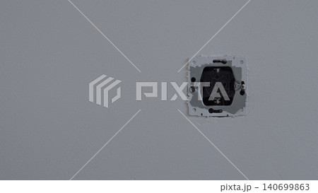 A single recessed electrical outlet opening is set into a plain gray interior wall, with exposed mounting edges and a minimal empty background under soft diffuse light A single recessed electrical outlet opening is set into a plain gray interior wall, with exposed mounting edges and a minimal empty background under soft diffuse light 140699863
