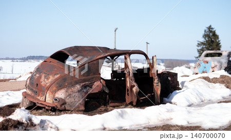 Corroded midcentury sedan shell abandoned on open rural field with melting snow patches; metal body heavily rusted with missing doors, windows, and interior Corroded midcentury sedan shell abandoned on open rural field with melting snow patches; metal body heavily rusted with missing doors, windows, and interior 140700070