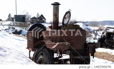 Antique rusted field stove mounted on small trailer parked in snow-covered rural yard, metal chimney and round lid open, worn wheels and corroded body showing Antique rusted field stove mounted on small trailer parked in snow-covered rural yard, metal chimney and round lid open, worn wheels and corroded body showing 140700076