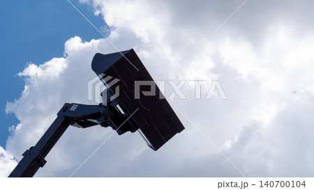 A black mechanical arm raises a rectangular panel into an open sky with bright clouds, creating a simple industrial silhouette and strong negative space 140700104
