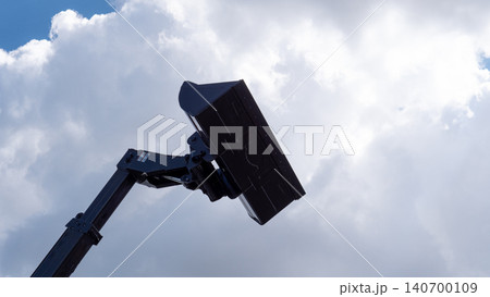 A low angle view of an excavator arm with a raised bucket silhouetted against a bright cloudy sky, showing heavy machinery, metal construction, and open outdoor space A low angle view of an excavator arm with a raised bucket silhouetted against a bright cloudy sky, showing heavy machinery, metal construction, and open outdoor space 140700109