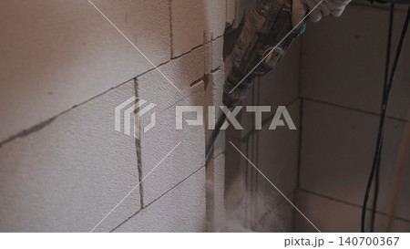 Electric Demolition Drill Breaking Block Wall, Heavy Dust Cloud, Gloved Hand Holding Power Tool, Interior Retrofit Scene, Fast Action, Rough Block Texture, Contractor Removing Material 140700367
