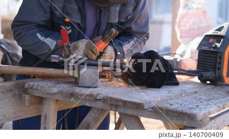 Worker Grinding Metal With Grinder, Sparks Flying Around Protective Gloves And Helmet, Closeup On Rotating Disc Cutting Steel On Dusty Workshop Bench, Hands Steadying Piece, Gritty Worker Grinding Metal With Grinder, Sparks Flying Around Protective Gloves And Helmet, Closeup On Rotating Disc Cutting Steel On Dusty Workshop Bench, Hands Steadying Piece, Gritty 140700409