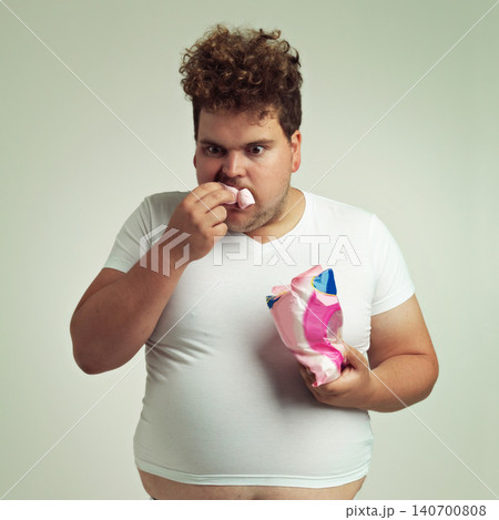Food, hungry and marshmallow with plus size man in studio on gray background for unhealthy eating. Hunger, appetite for sweets and ravenous young person with snack bag or packet for greed or gluttony 140700808