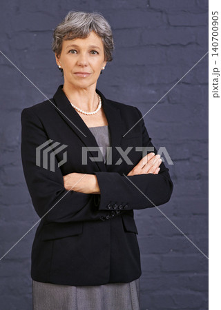 Mature woman, arms crossed and corporate professional with serious face, pride and ambition on wall background. Management, confidence in portrait and real estate agent in London with business 140700905