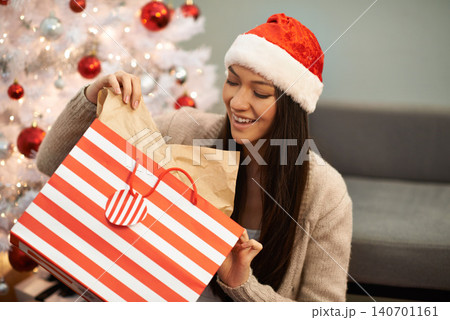Christmas gift, excited woman and bag in home for celebration of holiday or festive season with tree in living room. Xmas, happy person and open present with smile in lounge of apartment at party Christmas gift, excited woman and bag in home for celebration of holiday or festive season with tree in living room. Xmas, happy person and open present with smile in lounge of apartment at party 140701161