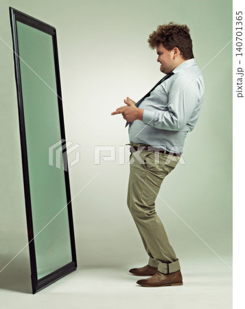 Man, mirror and plus size with reflection for confidence in body fat, fashion or outfit on a studio background. Young male person or big model in obesity, overweight or challenge on mockup space Man, mirror and plus size with reflection for confidence in body fat, fashion or outfit on a studio background. Young male person or big model in obesity, overweight or challenge on mockup space 140701365