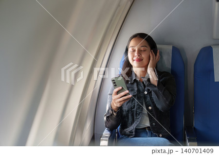 Asian woman listening to music with headphones on airplane flight 140701409