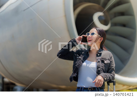 Asian woman talking on smartphone near airplane jet engine at airport 140701421