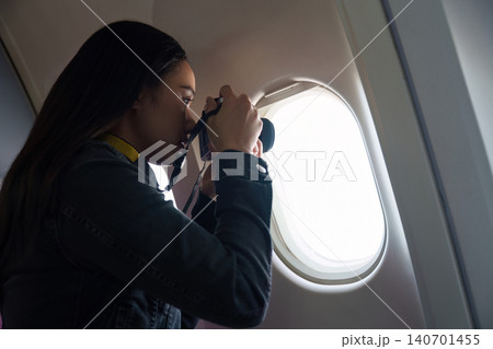 Asian woman photographing through airplane window with camera Asian woman photographing through airplane window with camera 140701455