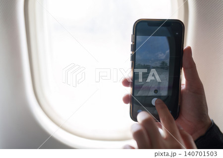 Cropped hands holding smartphone to take photo of view from airplane window during flight Cropped hands holding smartphone to take photo of view from airplane window during flight 140701503