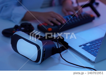 Hands typing on keyboard with virtual reality VR headset and laptop for immersive gaming technology Hands typing on keyboard with virtual reality VR headset and laptop for immersive gaming technology 140701951