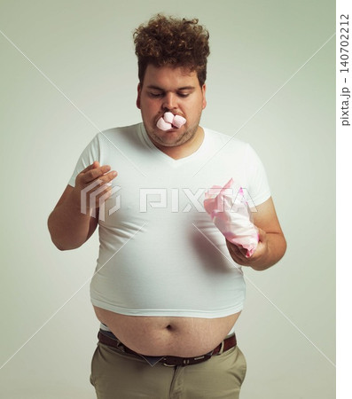 Obesity, weight gain and humor for man in studio with marshmallow for unhealthy eating, sugar and candy. Overweight person with sweets in mouth and fat stomach for greed, comedy and funny indoor 140702212