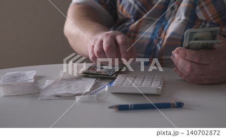 A person is sitting at a table, counting cash while looking at receipts. A calculator and a pen are nearby. It is a typical afternoon in a plain indoor environment. A person is sitting at a table, counting cash while looking at receipts. A calculator and a pen are nearby. It is a typical afternoon in a plain indoor environment. 140702872