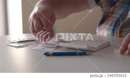 A person is reviewing receipts while using a calculator. Bills are placed on the table next to a pen. The setting is indoors with good lighting during daytime. A person is reviewing receipts while using a calculator. Bills are placed on the table next to a pen. The setting is indoors with good lighting during daytime. 140703012
