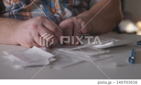 A person writes notes on various receipts and uses a calculator. The scene shows a cluttered table with papers and tools needed for managing expenses. 140703016