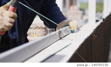 Closeup Worker Grinding Metal Railing With Angle Grinder, Gloved Hands Guiding Abrasive Wheel, Sparks Flying Against Concrete Ledge, Outdoor Construction Atmosphere, Focused Industrial Craft 140703156
