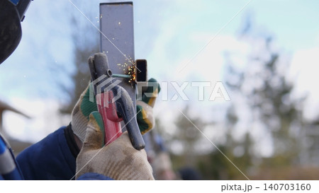 Close Up Welder Making Precision Seam Weld On Metal Post, Focused Hand Control, Clamp And Tape Visible, Bright Arc And Molten Bead, Safety Helmet Reflecting Sunlight, Meticulous Fabrication 140703160
