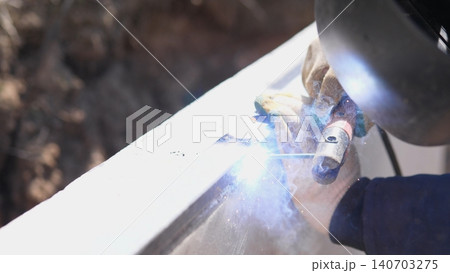 Welder In Protective Helmet Creating Intense Arc, Dramatic Sparks And Bright Blue Light Illuminate Gloves And Beam, Workshop Environment Emphasizes Safety, Control And Industrial Focus Welder In Protective Helmet Creating Intense Arc, Dramatic Sparks And Bright Blue Light Illuminate Gloves And Beam, Workshop Environment Emphasizes Safety, Control And Industrial Focus 140703275