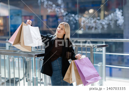 Woman smiling and holding many shopping bags in mall Woman smiling and holding many shopping bags in mall 140703335