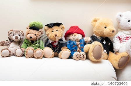 Collection of adorable teddy bears dressed in various outfits, showcasing unique styles and expressions, arranged neatly on a soft couch, perfect for children's decor or gifts 140703403