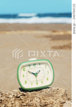 a green alarm clock on driftwood at the beach a green alarm clock on driftwood at the beach 140704132
